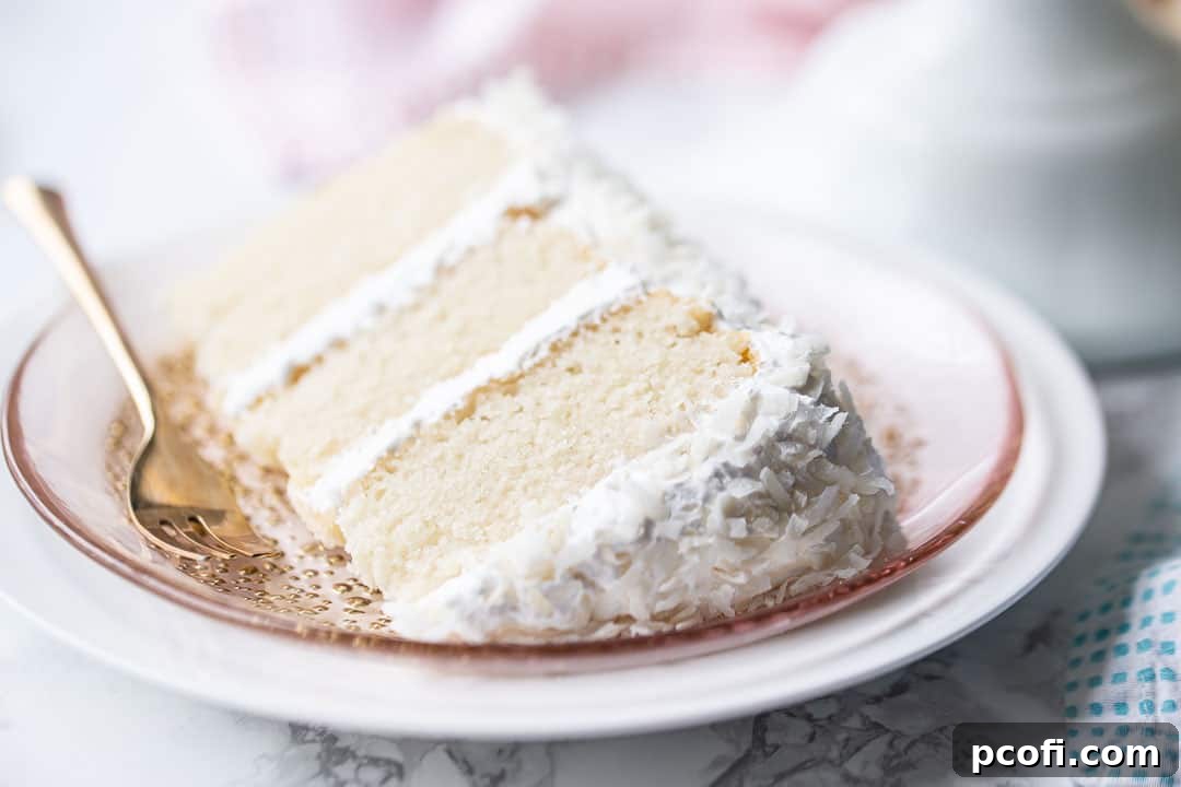 Best coconut cake recipe, baked and frosted with marshmallow frosting and coconut, sliced and served on its side, highlighting its irresistible layers.