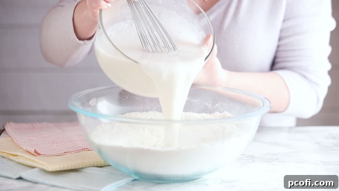 Pouring liquid ingredients into dry for coconut cake batter preparation, illustrating the careful combination of mixtures.