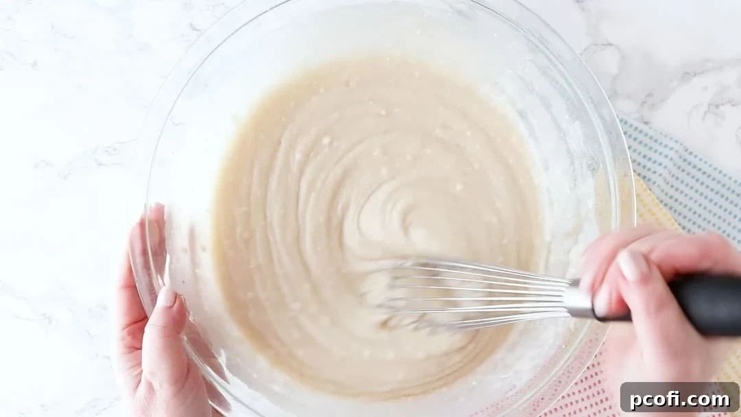 Whisking coconut cake batter in a large glass mixing bowl until just smooth, avoiding overmixing for a tender cake.