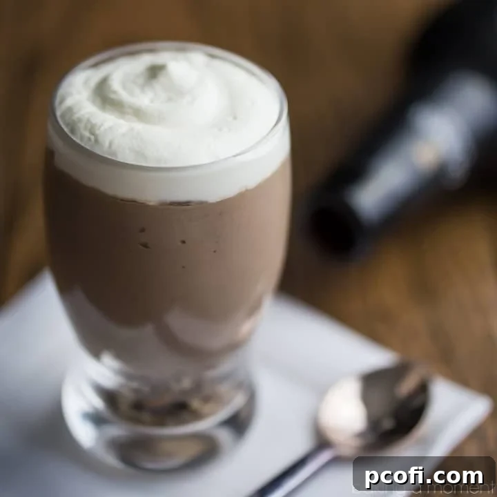 Mini beer glass of Guinness Chocolate Cheesecake Mousse, on a white napkin with a spoon and a bottle of Guinness Stout in the background. Capturing the rich chocolate and creamy texture.