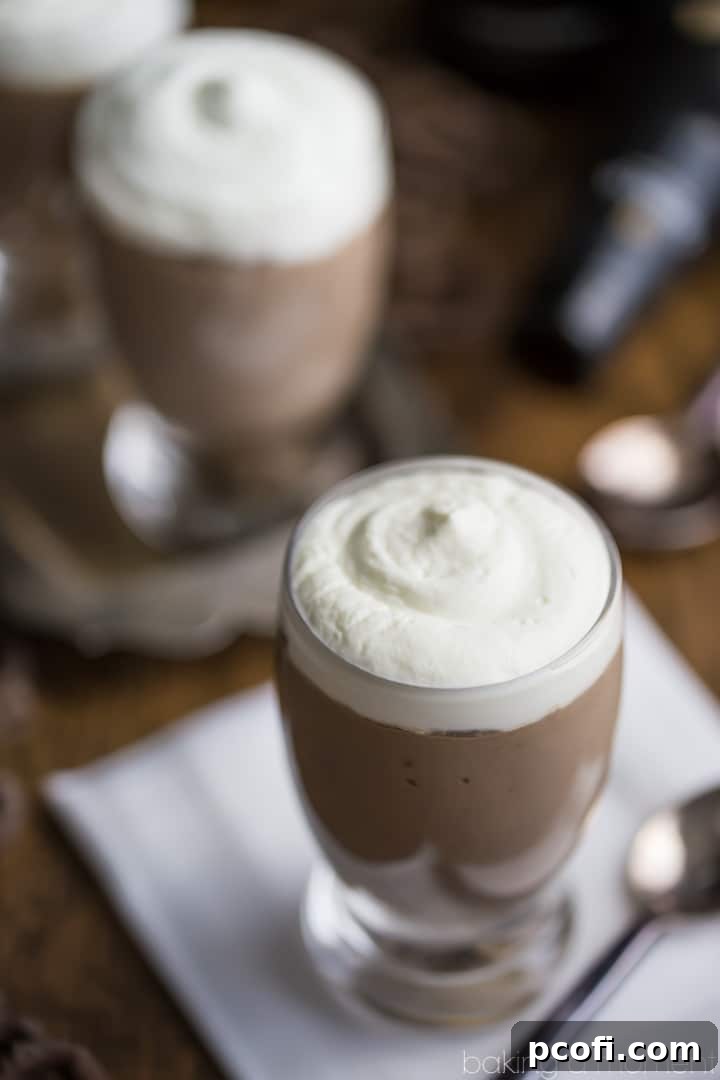 Close-up shot of a single mini beer glass filled with Guinness Chocolate Cheesecake Mousse, garnished with a dollop of whipped cream and a pretzel, placed on a white napkin next to a spoon and a blurred Guinness bottle. Emphasizing the creamy texture and appetizing presentation.