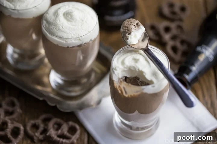 Overhead shot of several mini beer glasses of Guinness Chocolate Cheesecake Mousse, accompanied by spoons, bottles of Guinness Stout, and scattered chocolate covered pretzels in the background. Highlighting the ingredients and the finished dessert in a cohesive setup.