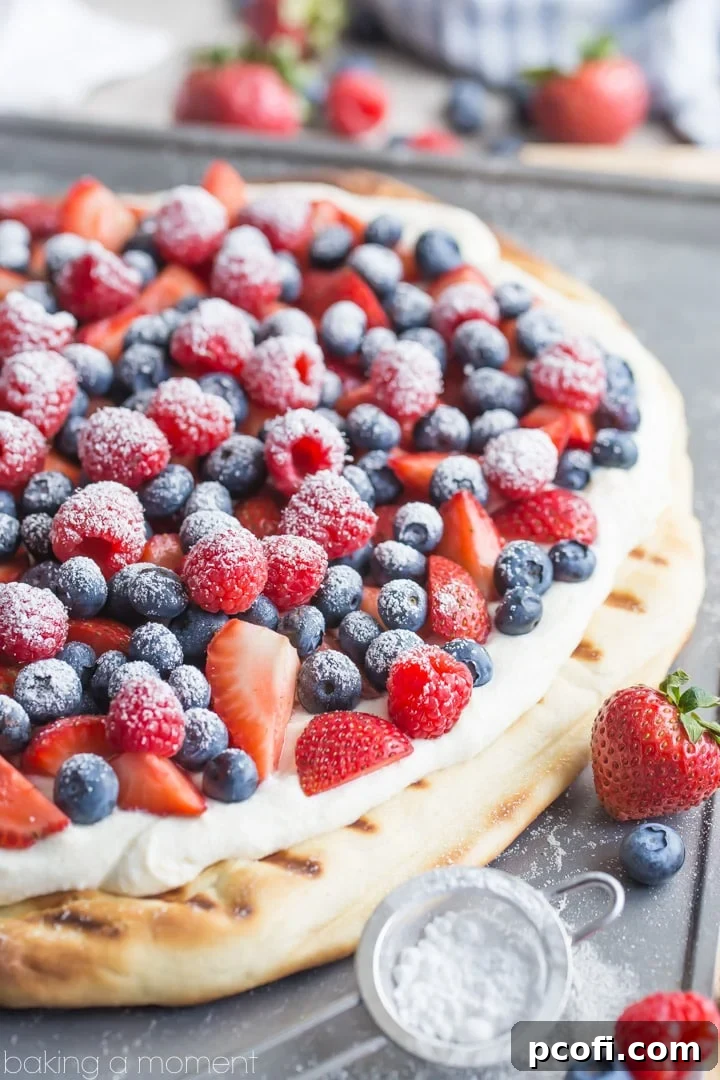 A selection of fresh, colorful summer berries including strawberries, blueberries, and raspberries, artfully arranged on a cooling grilled pizza crust with whipped ricotta.