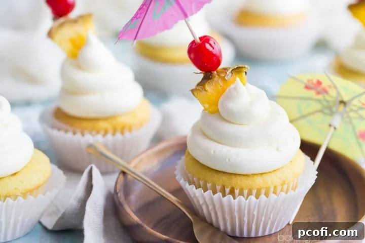 Four exquisitely decorated Pina Colada cupcakes arranged on a white cake stand, adorned with cherries, pineapple pieces, and tiny cocktail umbrellas, making a vibrant summer statement.