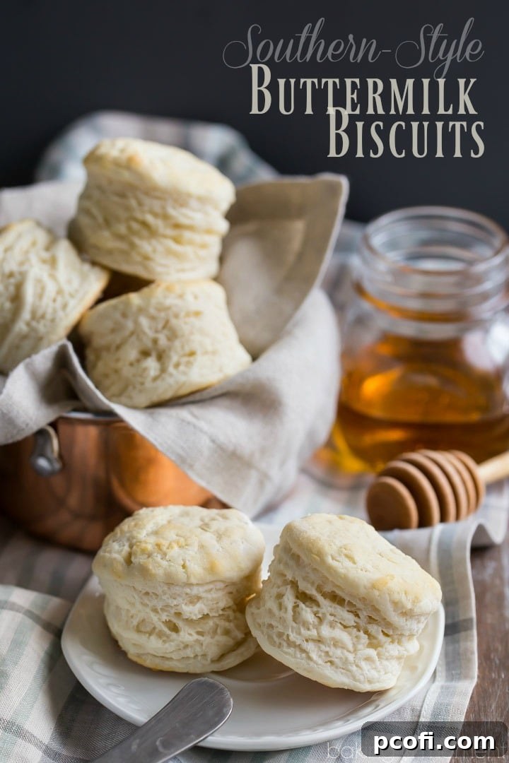Two buttermilk biscuits on an antique china plate, with a basket of biscuits and a jar of honey in the background.
