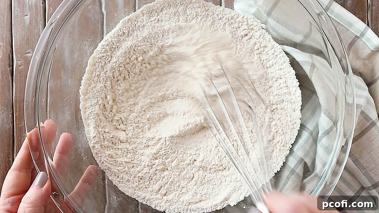 Flour, baking powder, and salt being stirred together in a large glass mixing bowl.