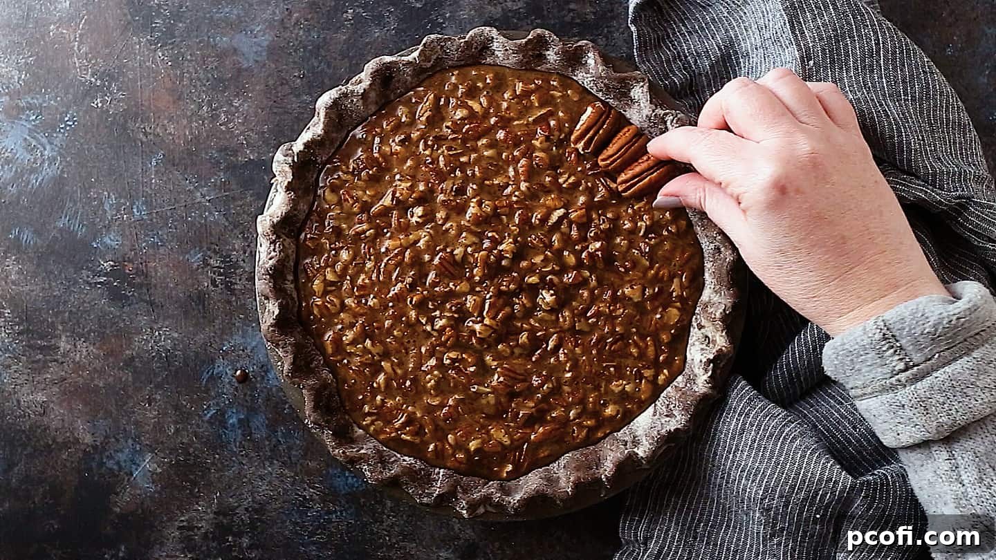 Garnishing the unbaked chocolate pecan pie with elegant pecan halves, artfully arranged on top of the rich filling, for a decorative finish.
