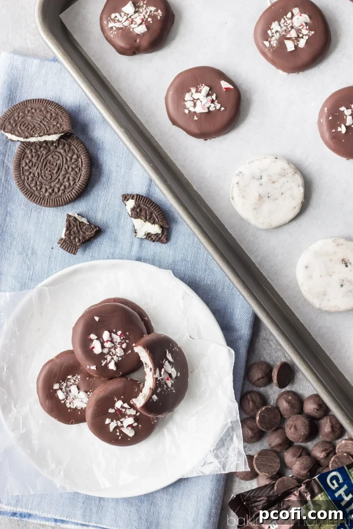 Freshly dipped cookies and cream peppermint patties, still wet with chocolate, being garnished with sprinkles of chopped peppermint bark.