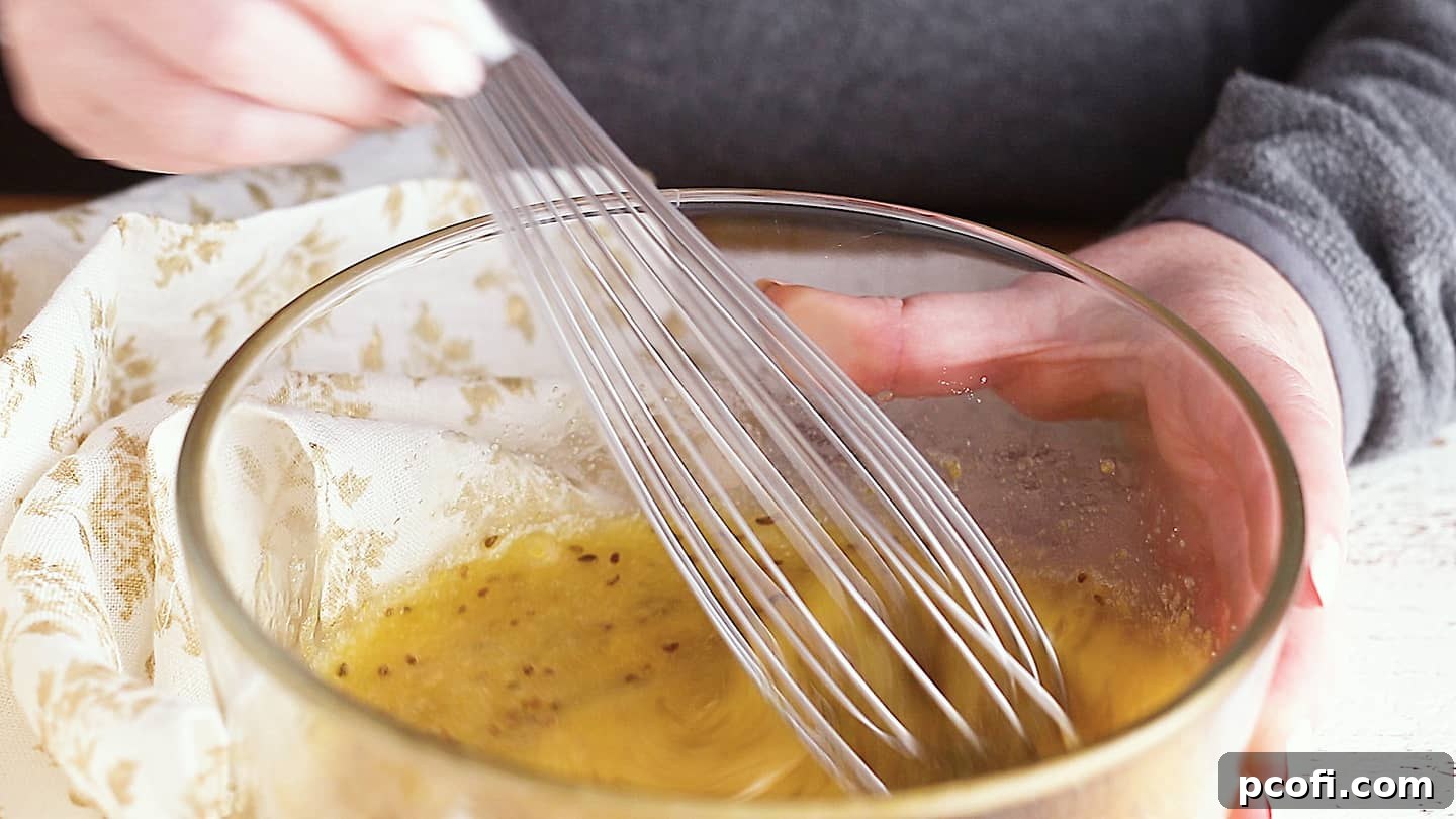 Stirring pizzelle ingredients together in a medium glass bowl with a wire whisk.