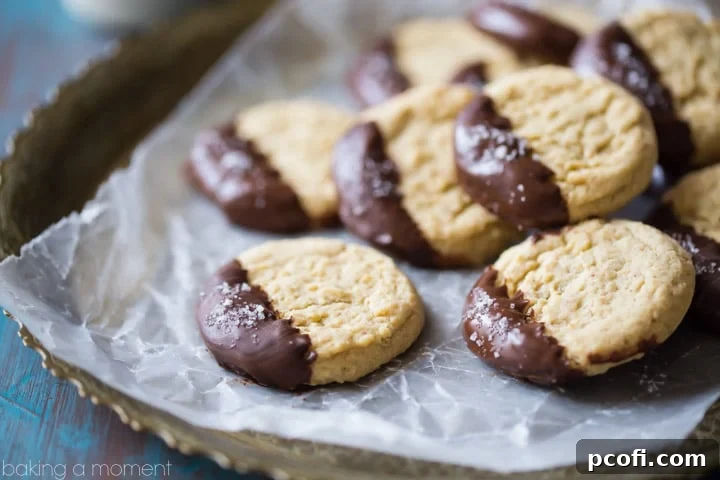 A beautifully arranged plate of freshly baked almond butter cookies, some elegantly dipped in dark chocolate and sea salt, glistening and ready to be served. A perfect dessert or delightful snack for any occasion.