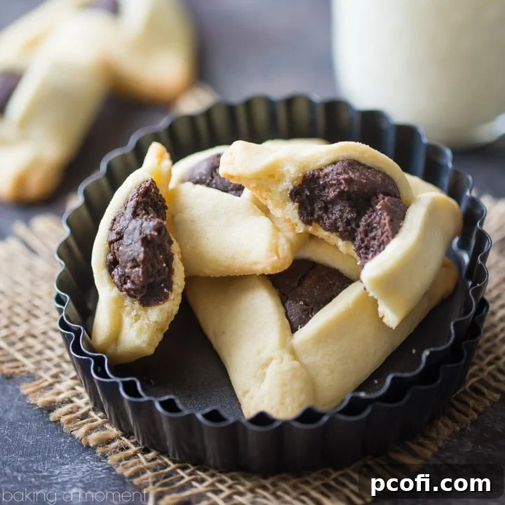 Fudge Brownie Hamantaschen - A close-up of a three-cornered sugar cookie filled with rich, dark chocolate brownie, sitting on a parchment-lined baking sheet. Perfect for Purim or any chocolate craving.