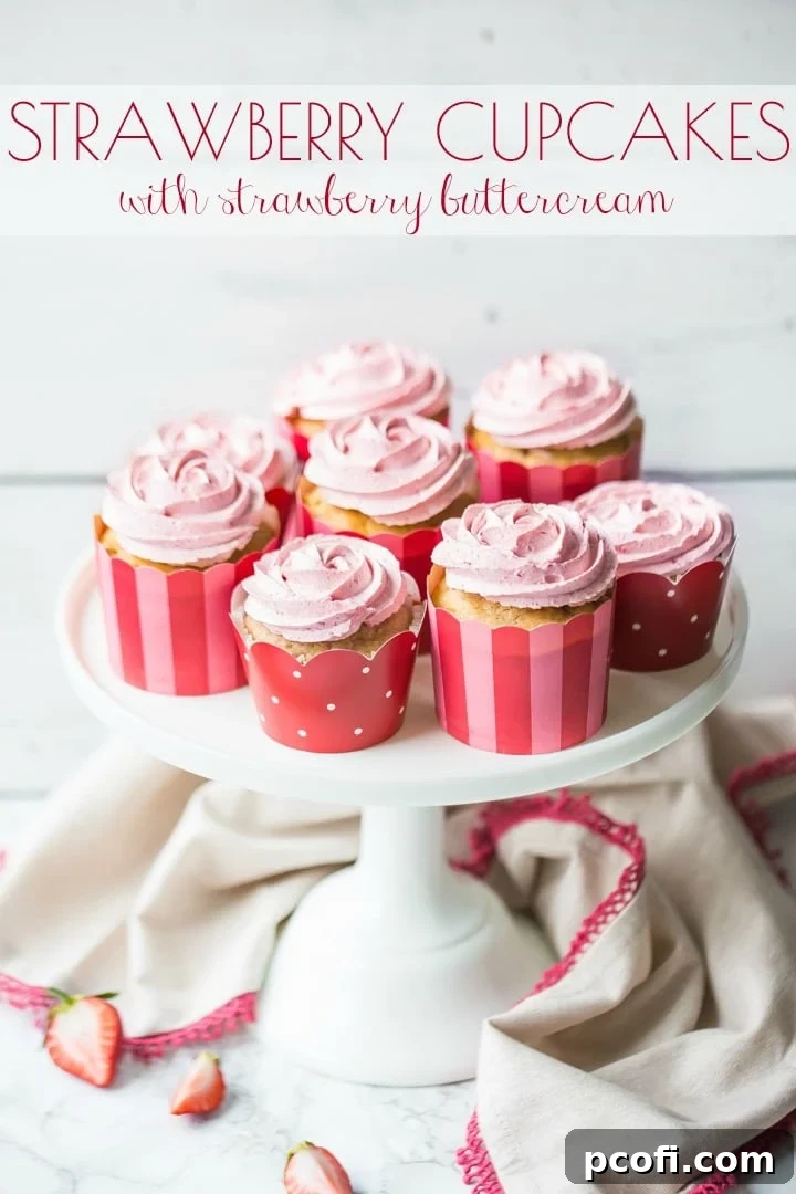A close-up of a beautifully frosted strawberry cupcake with strawberry buttercream, nestled in a festive pink, red, and white paper liner. The frosting forms an elegant rosette, ready to be enjoyed.