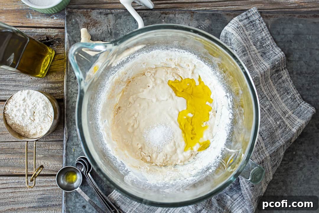 Adding essential olive oil and salt to the developing homemade pizza dough mixture.