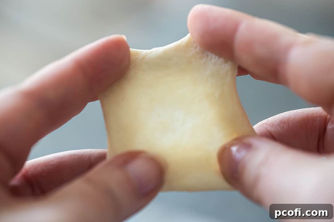 Performing the windowpane test on pizza dough, gently stretching a small piece until it's translucent enough to see light through without tearing.