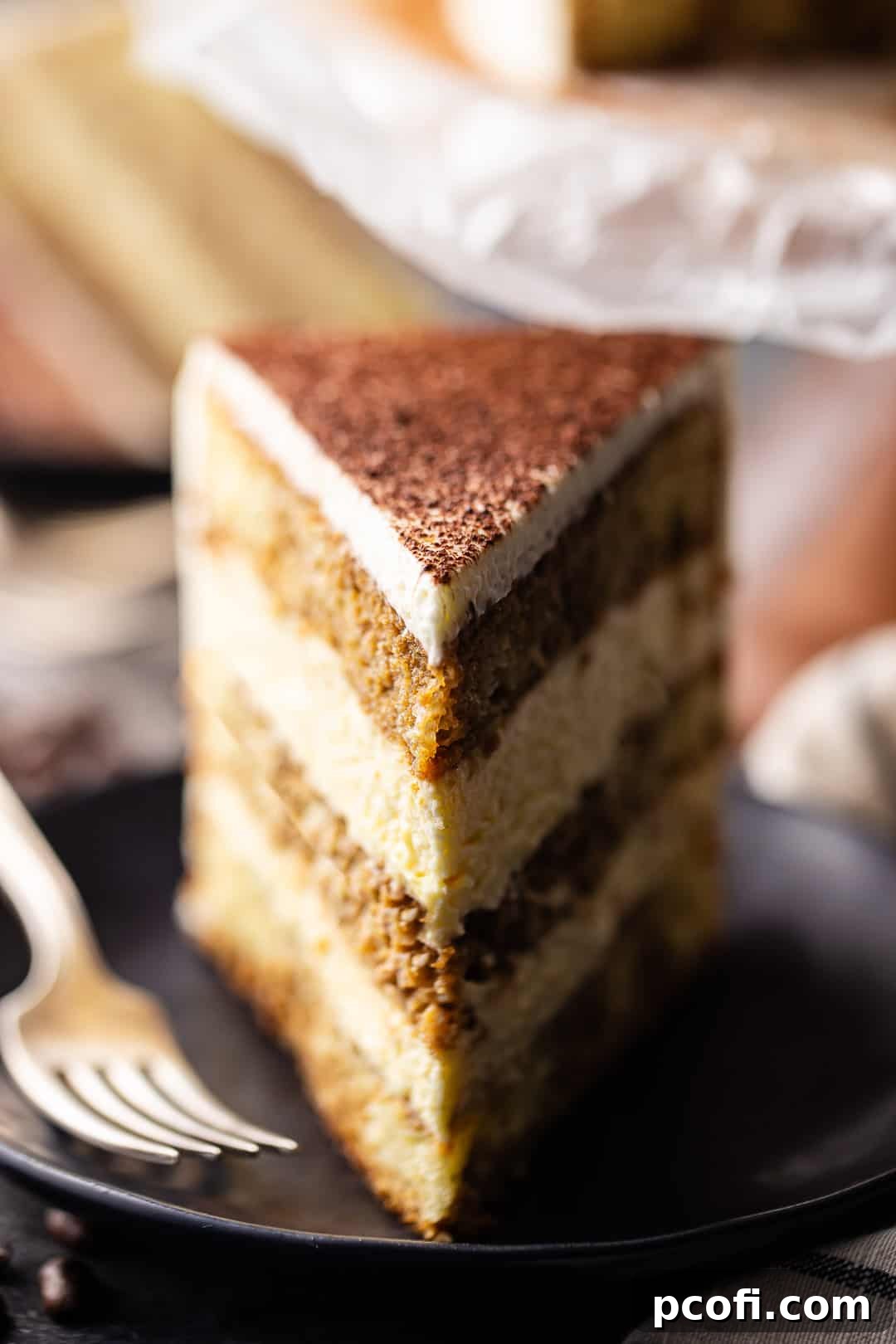 Tall slice of tiramisu cake on a dark plate with a vintage silver fork.