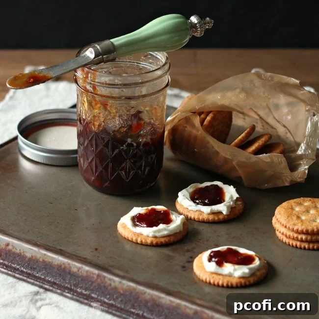 Tomato Jam in a glass jar with a spoon, showcasing its rich, thick texture