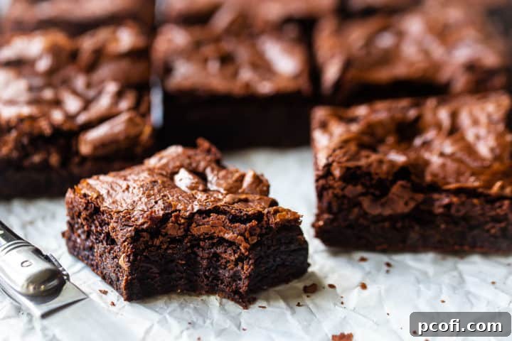 Brownies on white parchment, cut into squares with a sharp knife, with one bar in the foreground with a bite taken out of it.