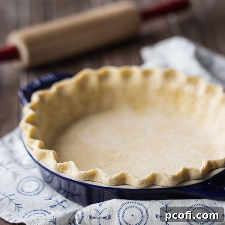 Unbaked pie crust in a dark blue pie dish, with a rolling pin in the background, ready for baking.