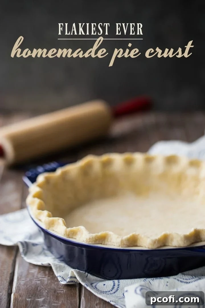 Vertical image of unbaked pie crust in a dark blue dish, with a rolling pin and flour in the background, highlighting readiness for baking.