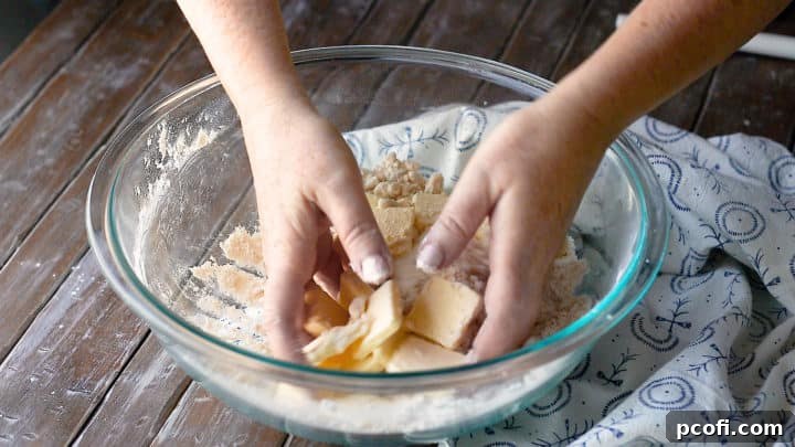 Tossing thin slices of cold butter with flour mixture by hand to coat each piece, preventing them from clumping together.
