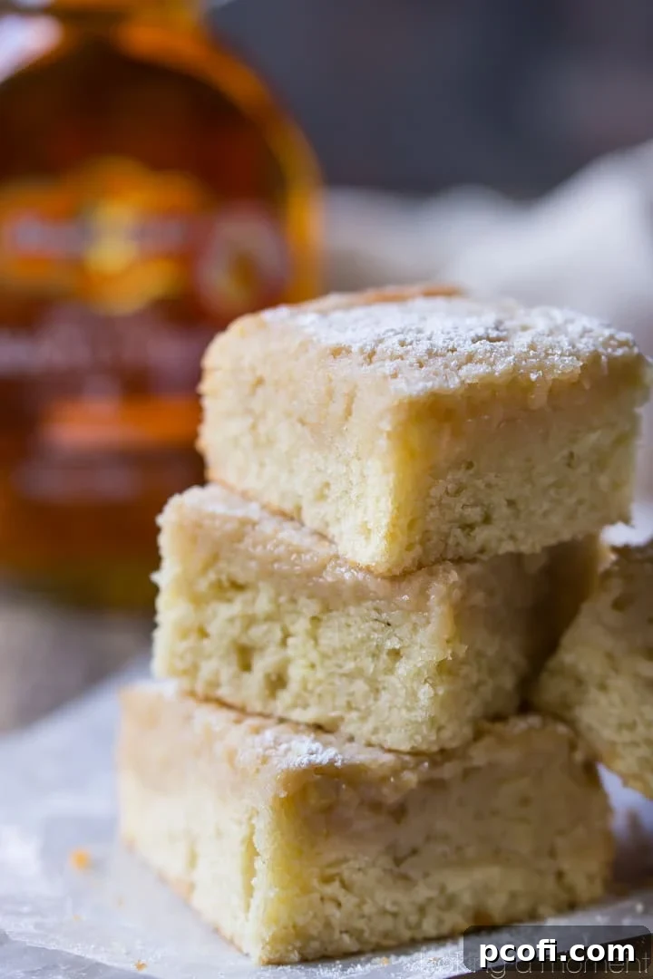 A slice of Maple Gooey Butter Cake on a white plate, showcasing the distinct layers of sturdy maple cake base and a thick, glossy, gooey maple topping.