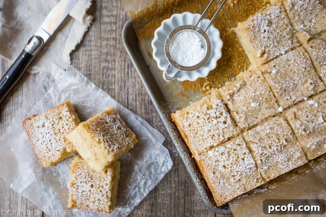 An overhead shot of Maple Gooey Butter Cake, cut into squares, with a light dusting of powdered sugar, ready to be served and enjoyed.