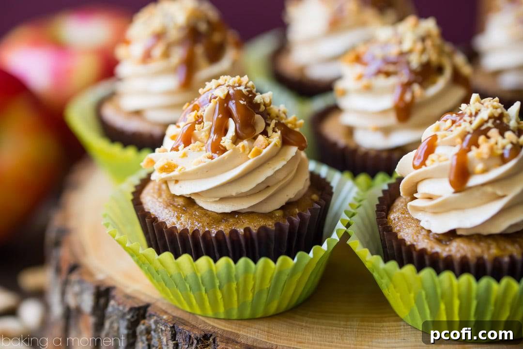 Caramel apple cupcakes displayed on a rustic wooden board, garnished with salted caramel buttercream, caramel drizzle, and chopped peanuts. Fresh whole apples and peanuts are in the background, reinforcing the fall theme and key ingredients. Keywords: food, desserts, apple, fall flavors, homemade cupcakes.