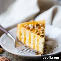 Slice of caramel pecan cheesecake on a plate, drizzled with caramel sauce and sprinkled with chopped pecans.