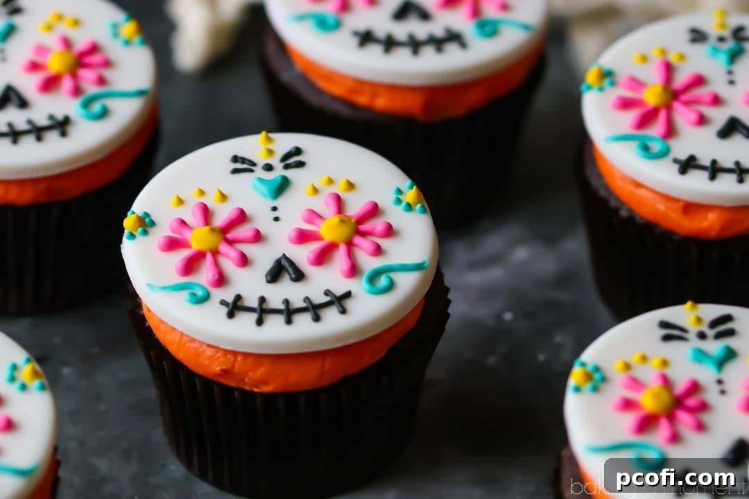 Close-up of a finished Day of the Dead cupcake featuring a multi-colored sugar skull fondant topper on a dark chocolate cupcake with bright orange frosting. Perfect for festive Halloween celebrations.