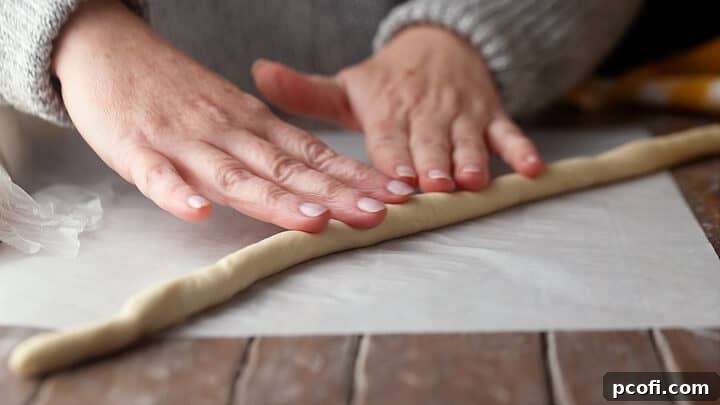 Hands carefully rolling a portion of soft pretzel dough into a long, slender rope on a clean countertop.