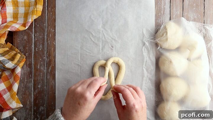 Hands demonstrating the intricate twisting of soft pretzel dough into its classic, symmetrical shape.