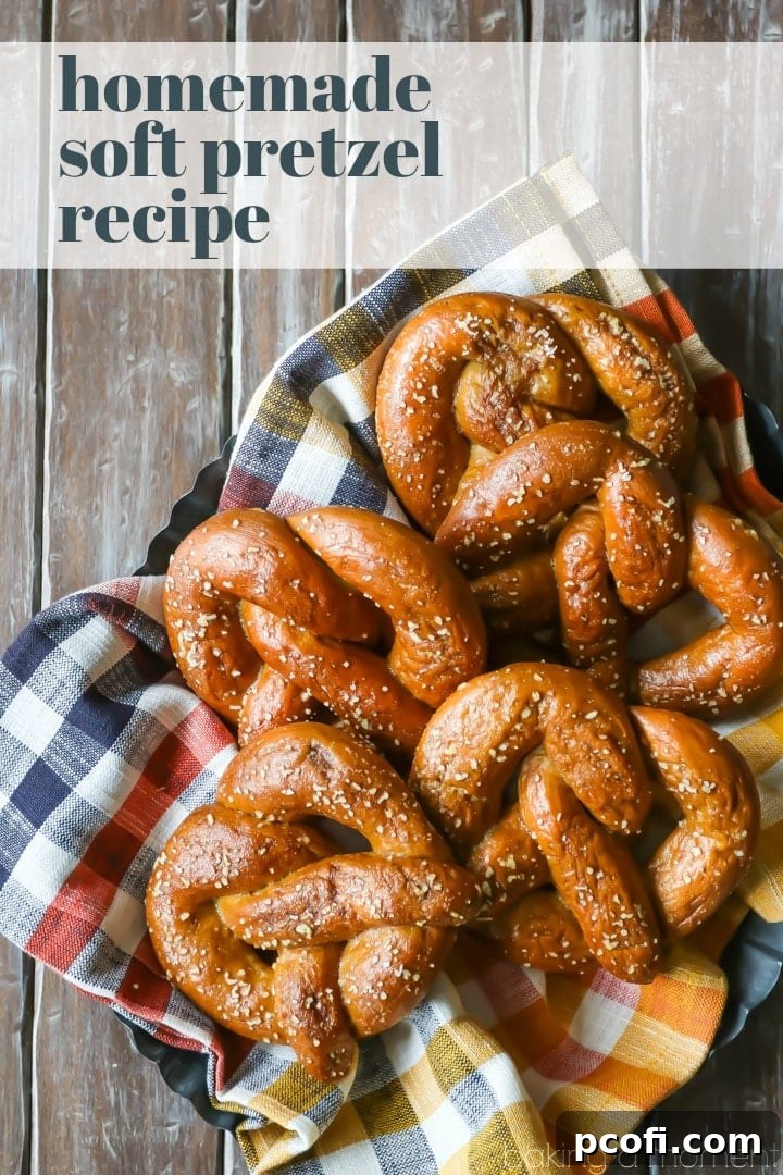 A perfectly baked homemade soft pretzel, golden-brown and glistening with salt, resting on a rustic plaid napkin, ready for dipping.