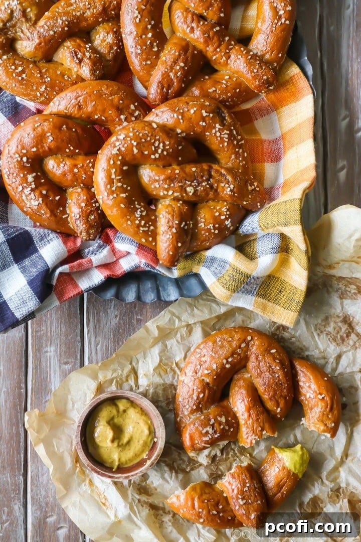 A freshly baked homemade soft pretzel, expertly torn into smaller pieces, served alongside a bowl of rich brown mustard for dipping.
