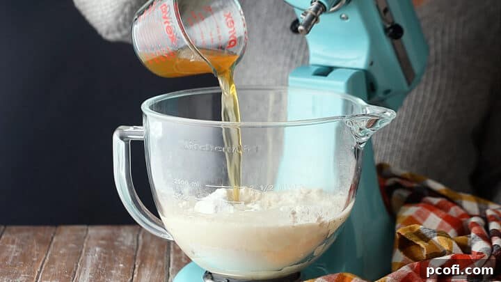 A stand mixer bowl with the foamy yeast mixture, along with bread flour, kosher salt, and beer being added to form the pretzel dough.
