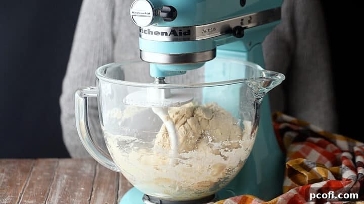 A stiff, yet perfectly formed ball of pretzel dough in a stand mixer, indicating proper consistency for kneading.