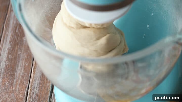 Pretzel dough being kneaded in a stand mixer, demonstrating its transformation into a silky and elastic consistency.