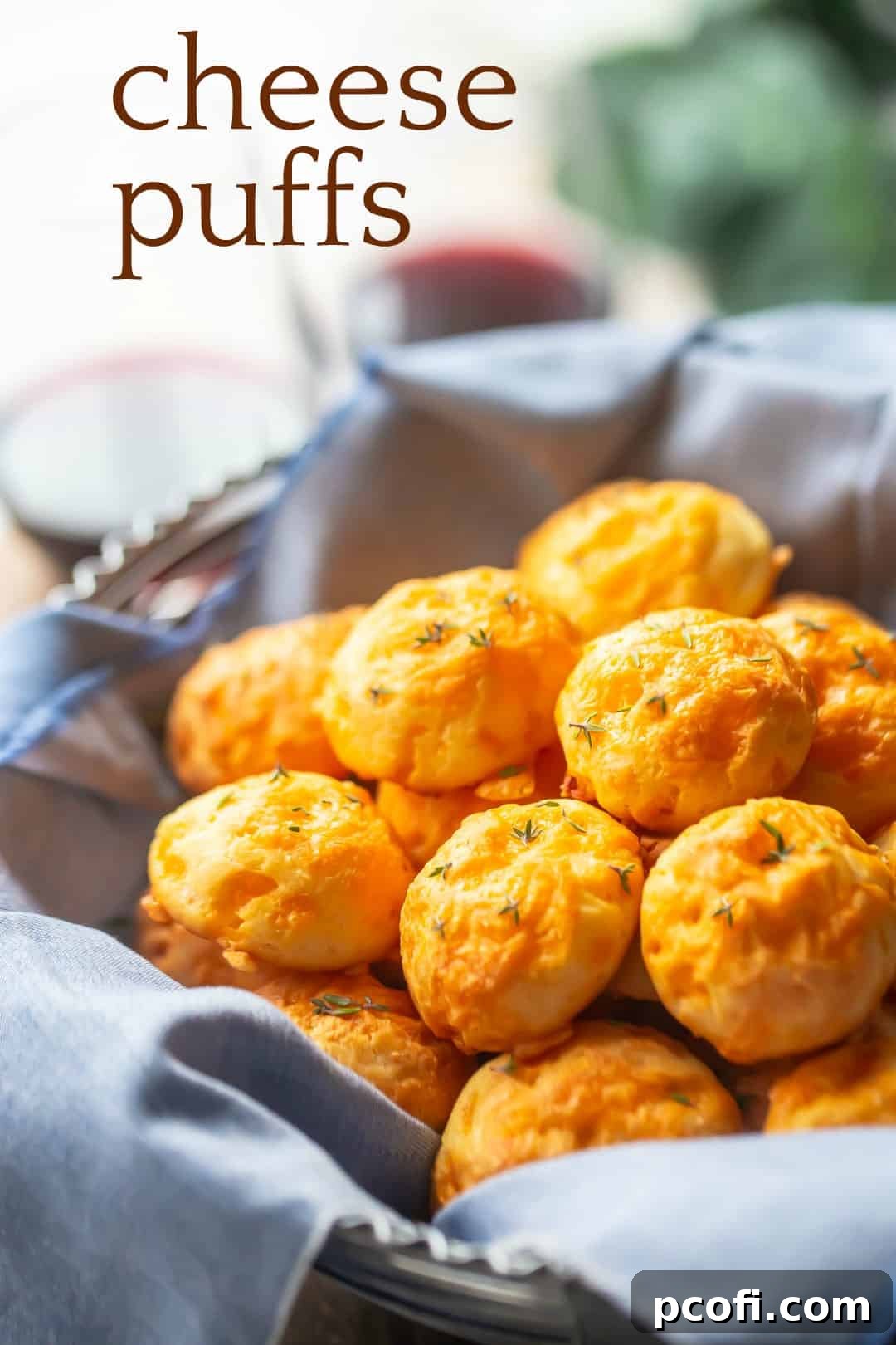 A charming basket filled with fluffy Gougeres, accompanied by a blue napkin, with a text overlay reading "Cheese Puffs."