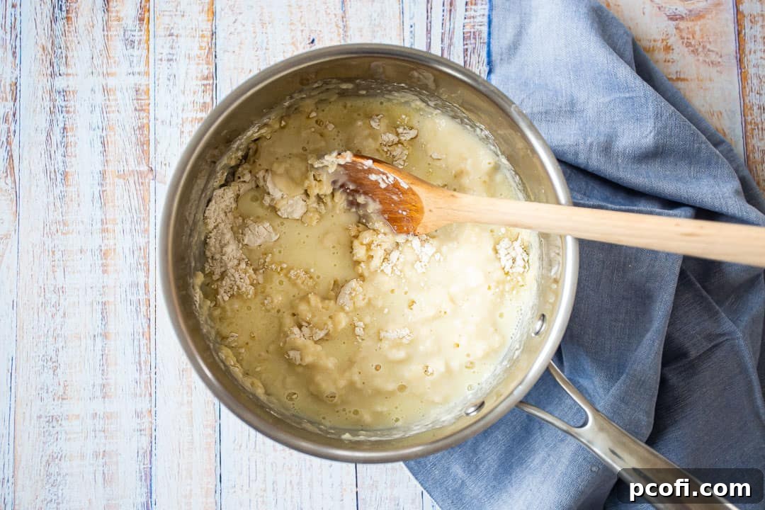 A wooden spoon stirring flour into the liquid in a saucepan, beginning to form the pate a choux dough.