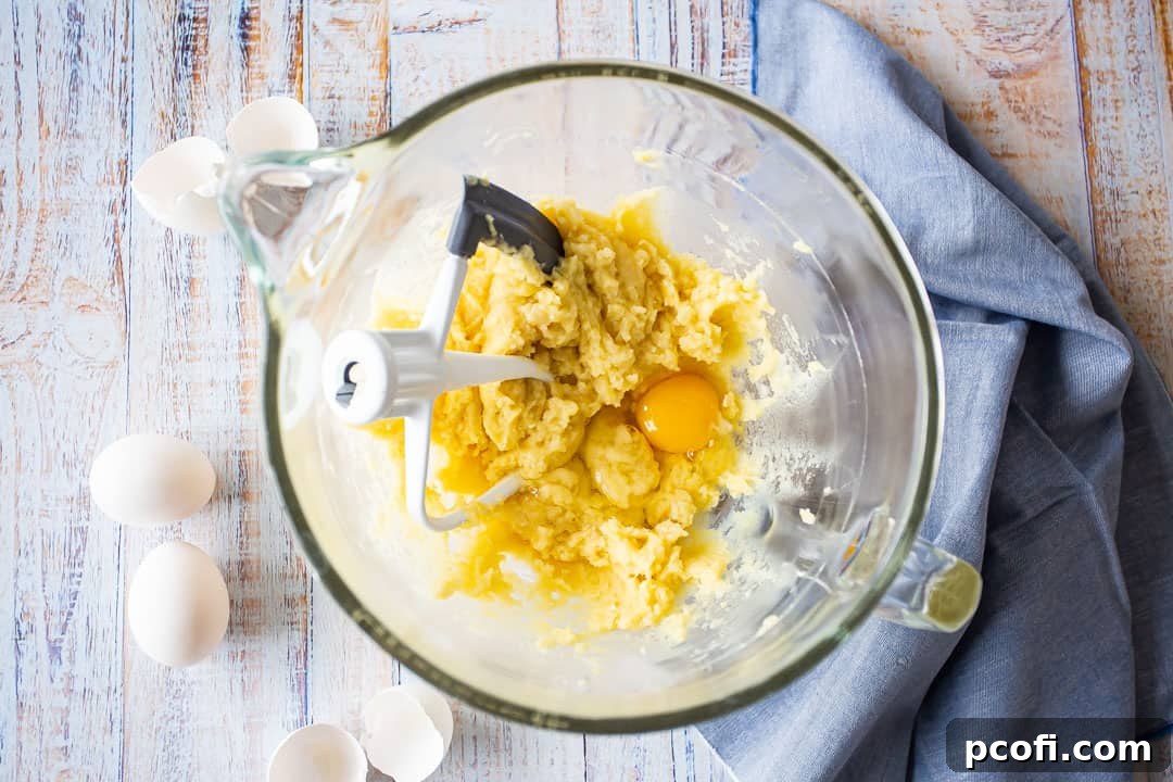 Adding an egg to the pate a choux dough in a mixing bowl, prior to full incorporation.