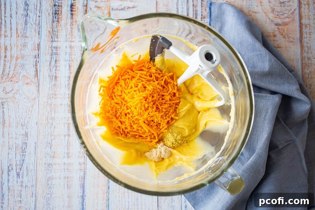 Cheese and spices being folded into the gougeres batter in a mixing bowl.
