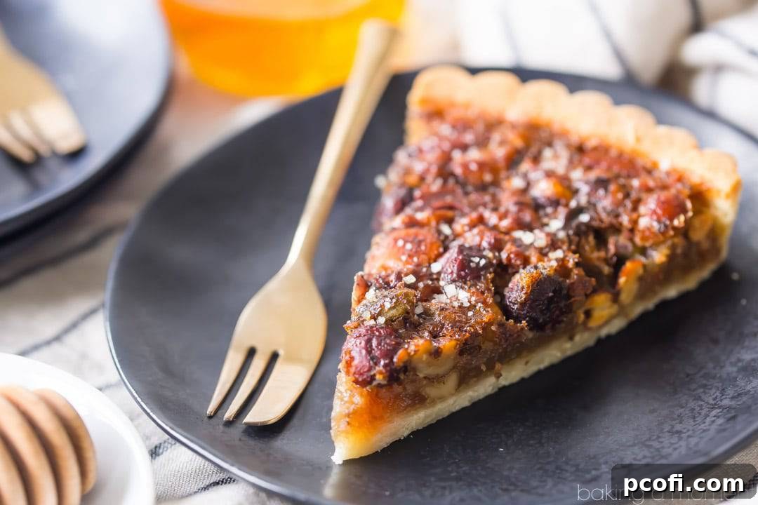 A slice of honey nut tart on a dark plate with gold fork and jar of honey in background.