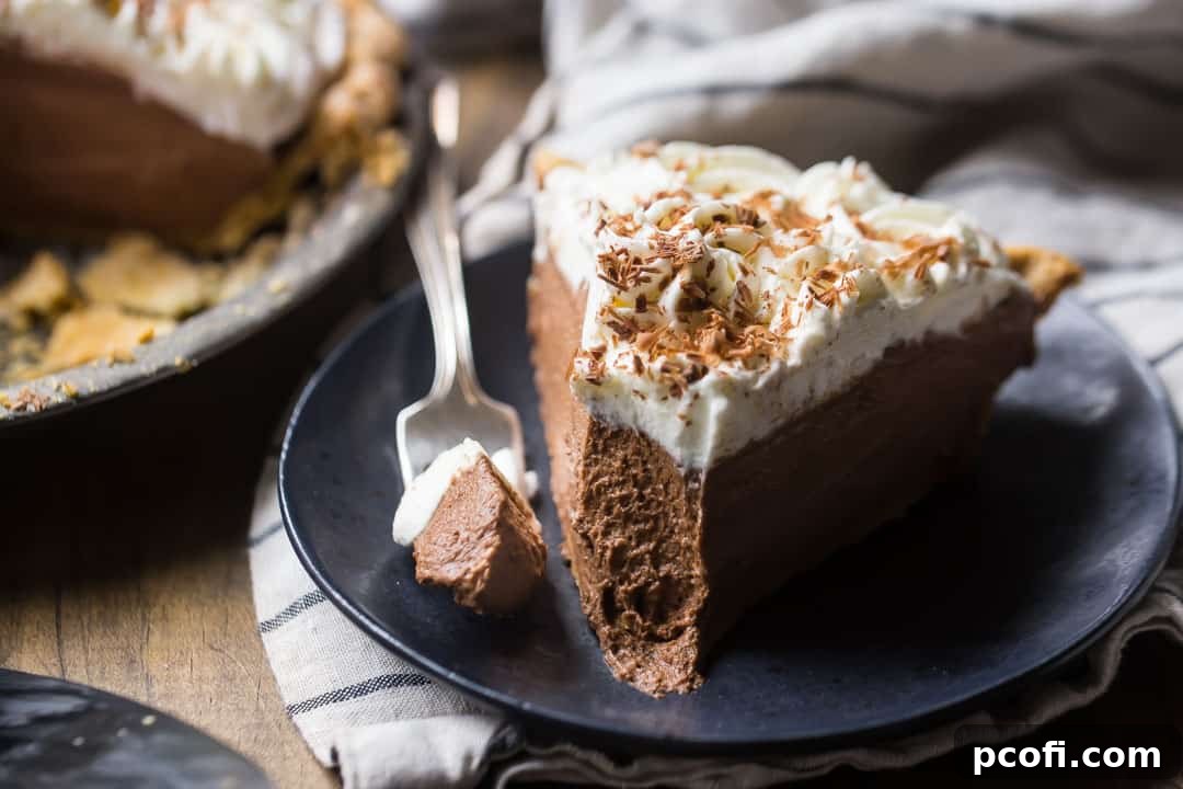 A delectable slice of chocolate cream pie, with a perfect bite removed, rests on a dark wood background, showcasing its inviting layers of crust, mousse, and whipped cream.