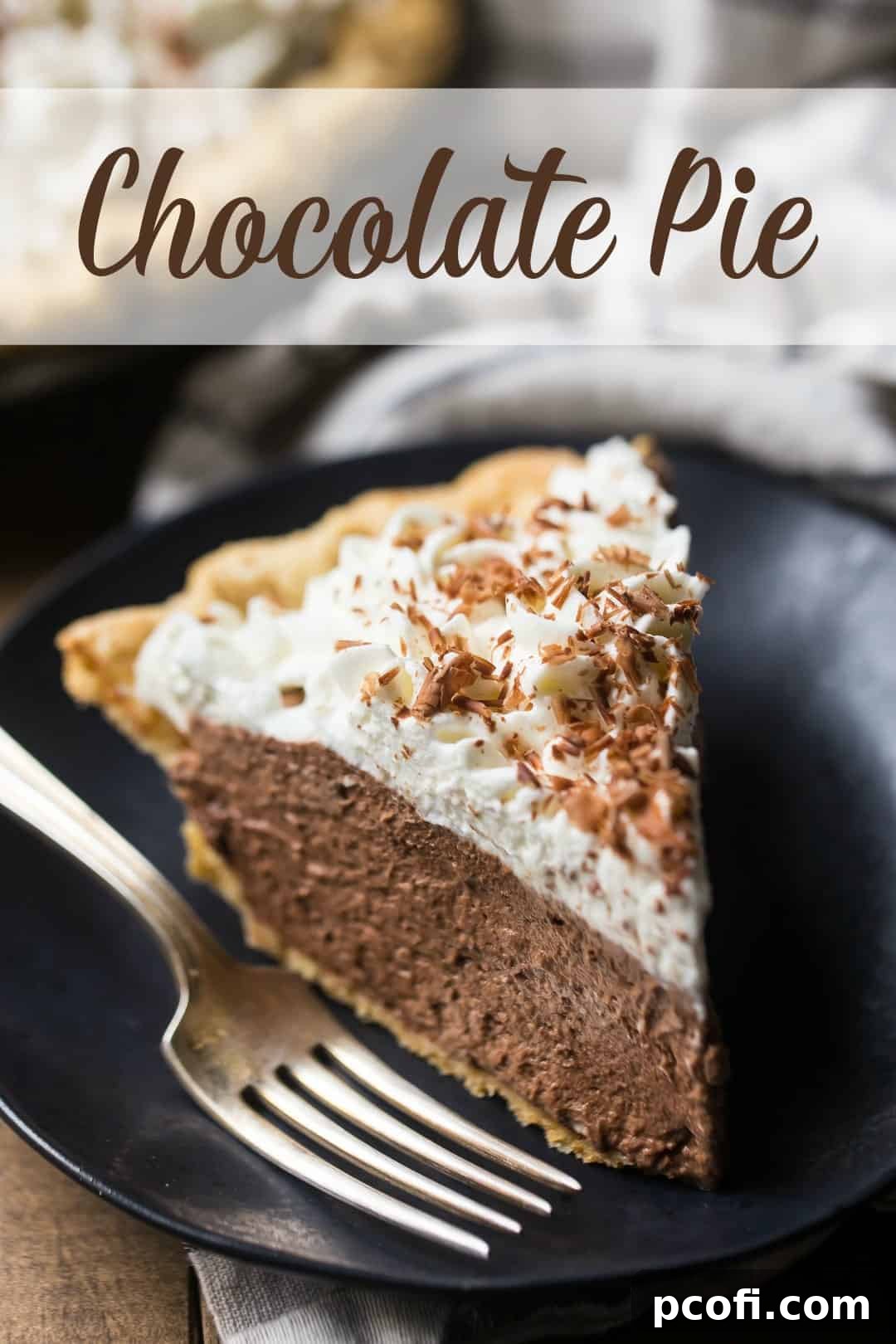 Close-up view of a generously sized slice of chocolate pie on a dark plate, accompanied by a silver fork, highlighting the creamy texture and inviting appeal. The top layer of whipped cream is sprinkled with chocolate shavings.