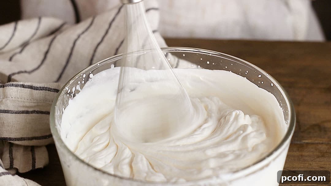 Heavy cream is being vigorously whipped in a clear glass bowl using an electric mixer, achieving a stiff and airy consistency perfect for folding into the chocolate filling.