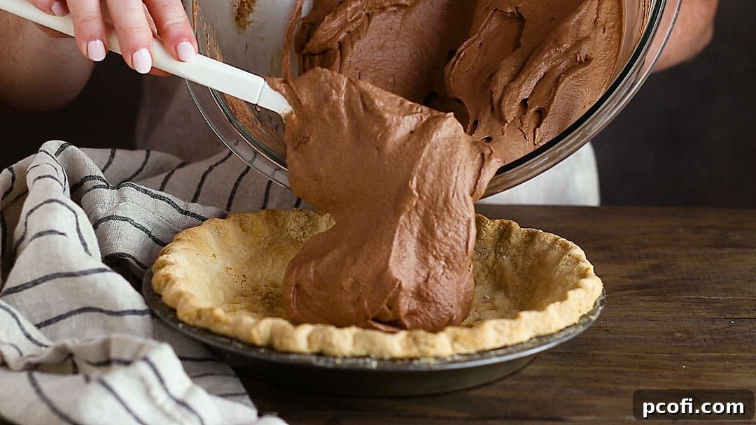 A pie crust is being carefully filled with the fluffy chocolate cream pie filling, ensuring an even distribution and smooth surface.