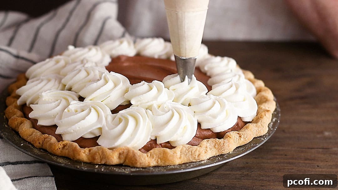 Elegant rosettes of sweetened whipped cream are being piped artfully onto the surface of the chilled chocolate pie, adding a luxurious and visually appealing topping.