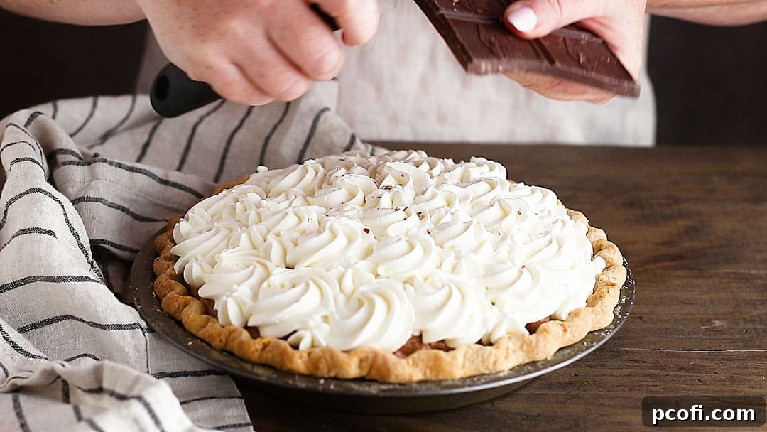 Delicate chocolate shavings are being scattered over the whipped cream topping of a chocolate pie, serving as a beautiful and delicious garnish that enhances its appeal.