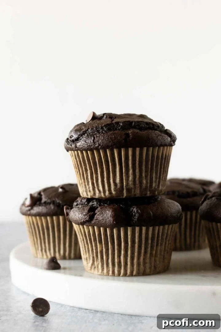 A charming display of stacked chocolate pumpkin muffins, still in their paper liners, presented on an elegant marble tray, hinting at their rich, moist texture and seasonal flavor.
