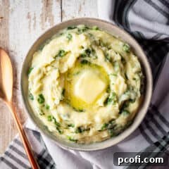 Cheesy Colcannon in a serving bowl with a pat of butter melting on top, garnished with fresh herbs.