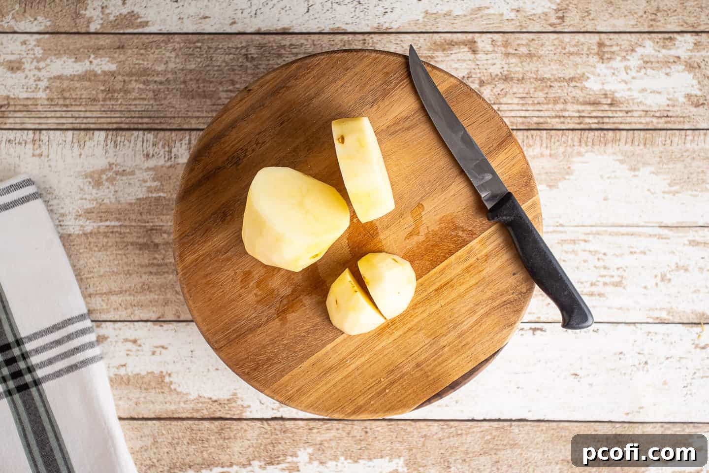 Peeled russet potatoes being cut into uniform chunks on a wooden cutting board, ready for boiling.